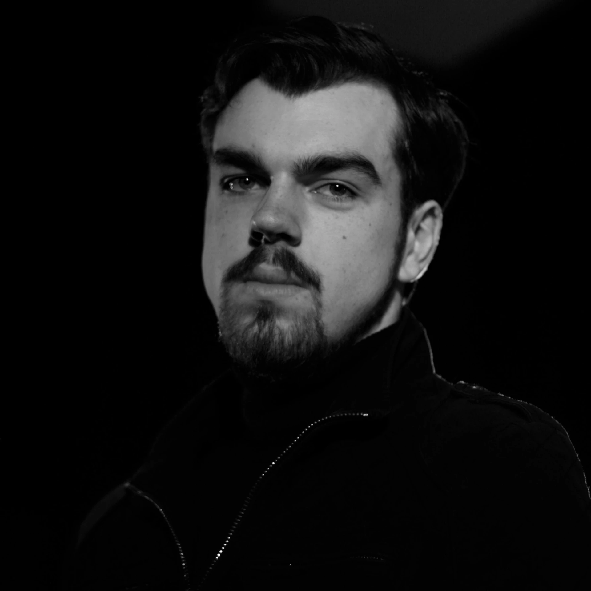 a black and white photo of a man with a beard, an album cover, unsplash, tom burke, ethan van sciver, a man wearing a black jacket, dark. no text
