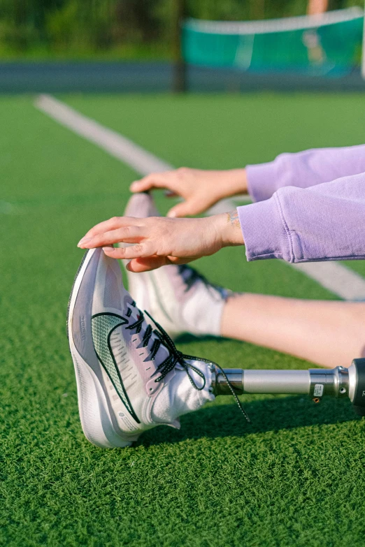 a woman sitting on top of a tennis court next to a racquet, trending on pexels, stretching her legs on the grass, sitting in a wheelchair, on a football field, pastel'