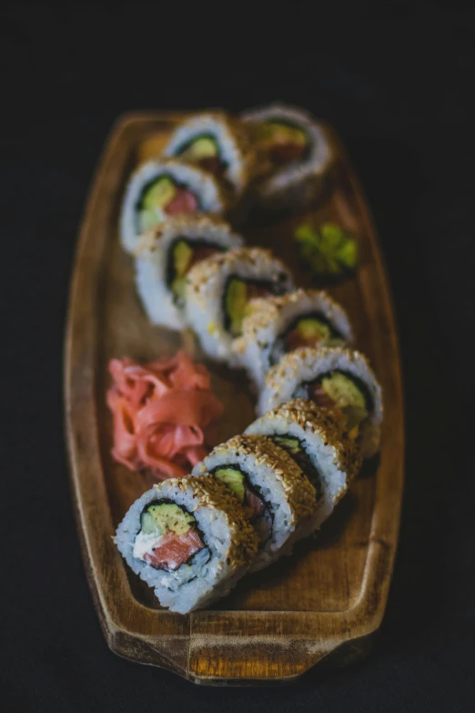 a wooden plate topped with sushi on top of a black table, paul barson, highly upvoted, gold, pastel'