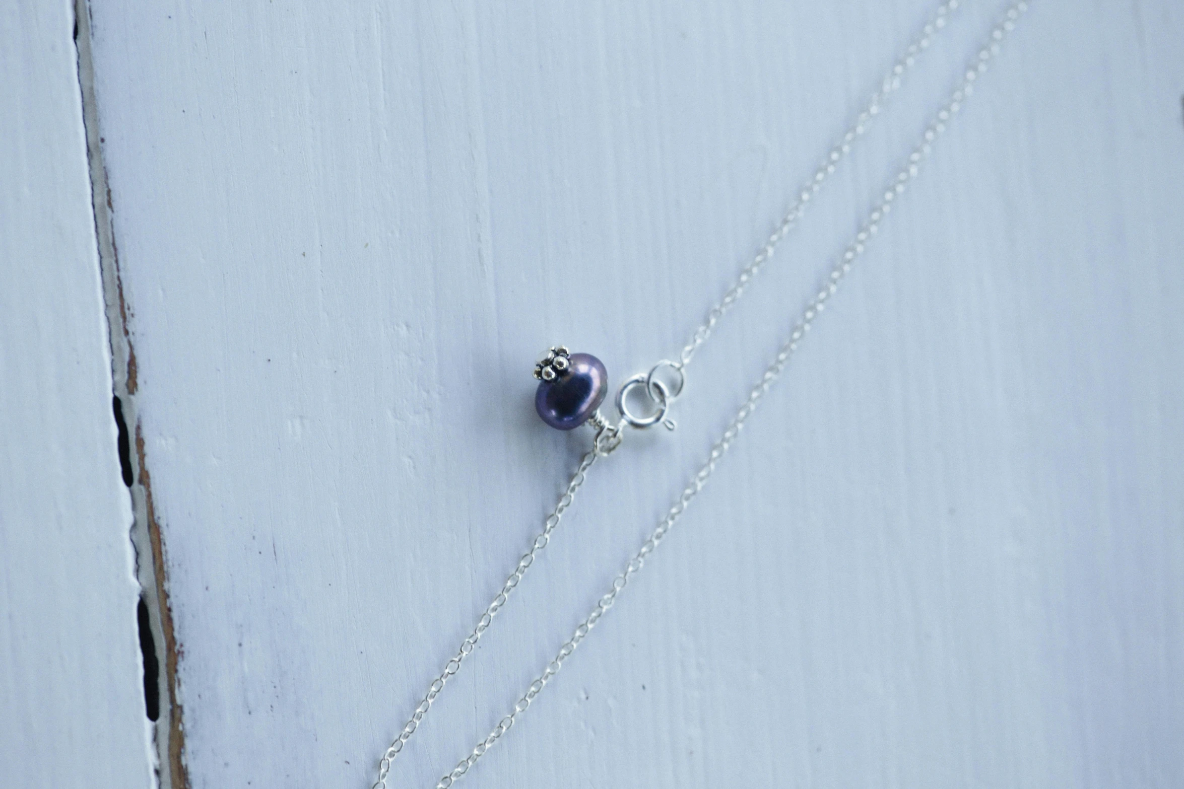 a close up of a necklace on a wooden surface, inspired by Perle Fine, hurufiyya, blueberry, small, low detail, pearl silverplate