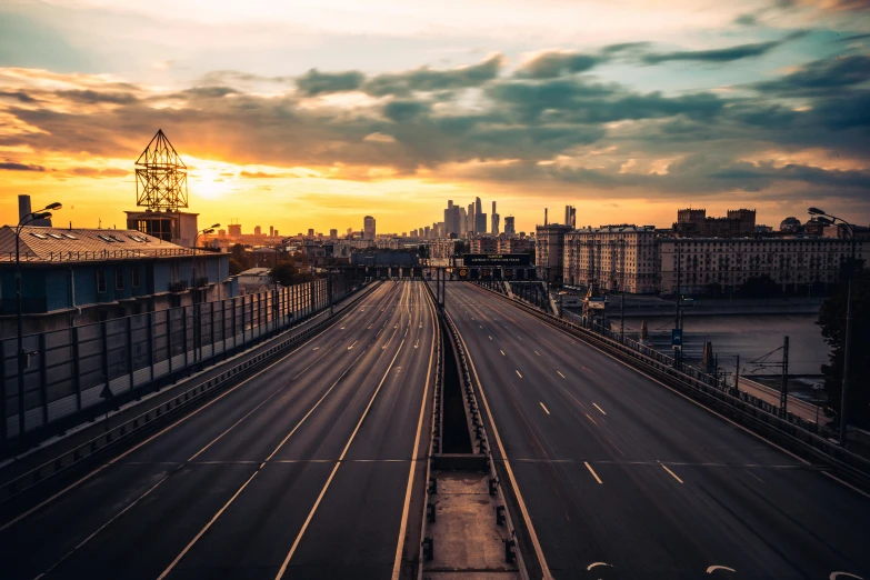 a train traveling down a train track next to a city, by Andrei Kolkoutine, pexels contest winner, highway and sunset!!, street of moscow, wide roads, we go