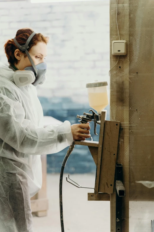 a woman in a lab coat using a spray gun, by artist, respirator, thick paint, worksafe.2000s, cardboard