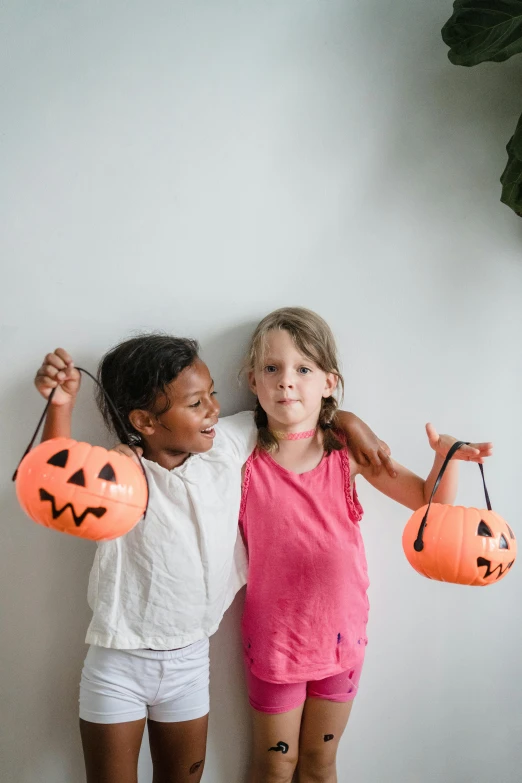 two little girls standing next to each other holding pumpkins, pexels contest winner, happening, paper cutouts of plain colors, hanging lanterns, 256435456k film, diverse