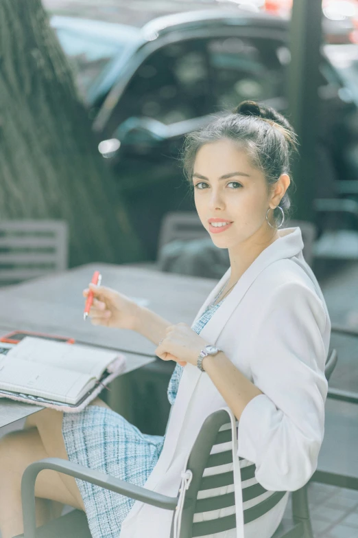 a woman sitting at a table with a laptop, pexels contest winner, wearing lab coat and a blouse, handsome girl, holding pencil, al fresco