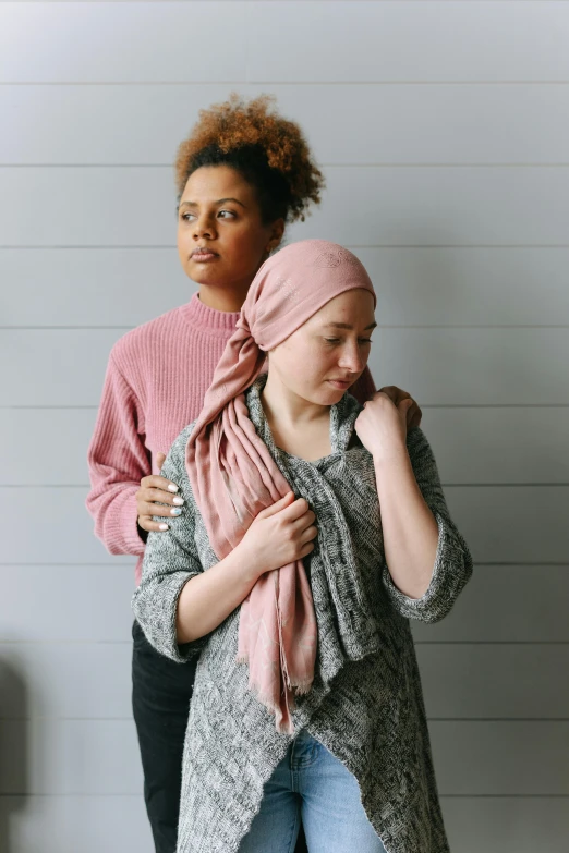 two women standing next to each other wearing scarves, by Winona Nelson, bald, tumours, praying, arm around her neck