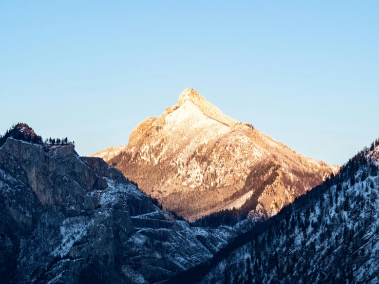 a large mountain covered in snow next to a forest, unsplash contest winner, post-impressionism, morning light showing injuries, clear blue skies, spire, colorado