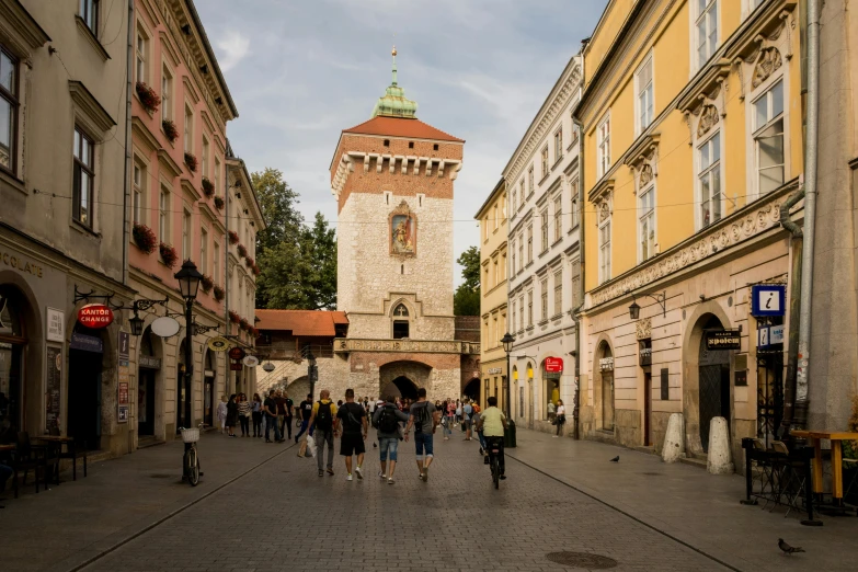 a group of people walking down a street next to tall buildings, by Emma Andijewska, pexels contest winner, graffiti, medieval gates, poland, square, summer evening