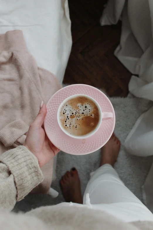 a person sitting on a bed holding a cup of coffee, some pink, creamy, full of people, instagram post