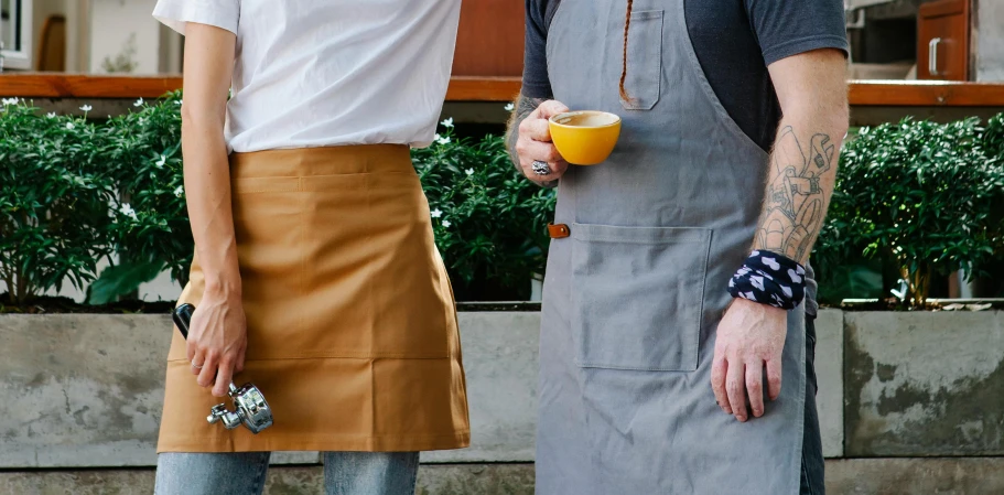 a man and a woman standing next to each other, inspired by Gordon Browne, unsplash, starbucks aprons and visors, ochre, pockets, medium close up