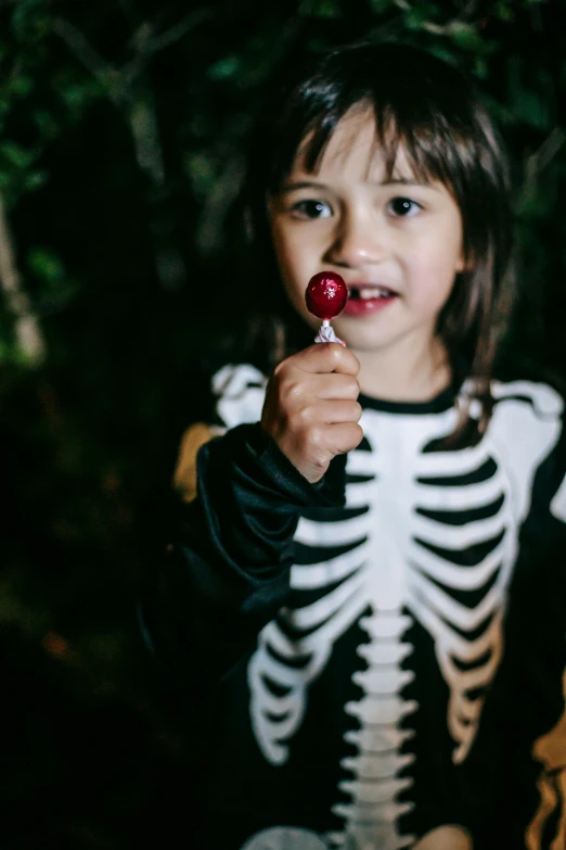 a little girl in a skeleton costume holding a candy, pexels, in the dark forest, and, profile image, kid