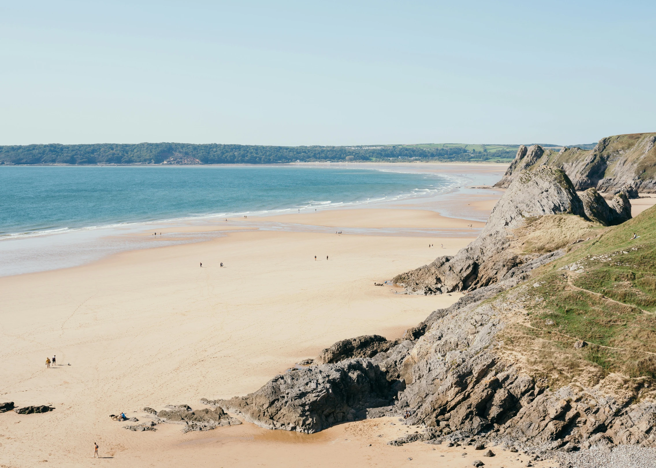 a group of people standing on top of a sandy beach, by Arabella Rankin, pexels contest winner, les nabis, coastal cliffs, omaha beach, hills and ocean, on a bright day