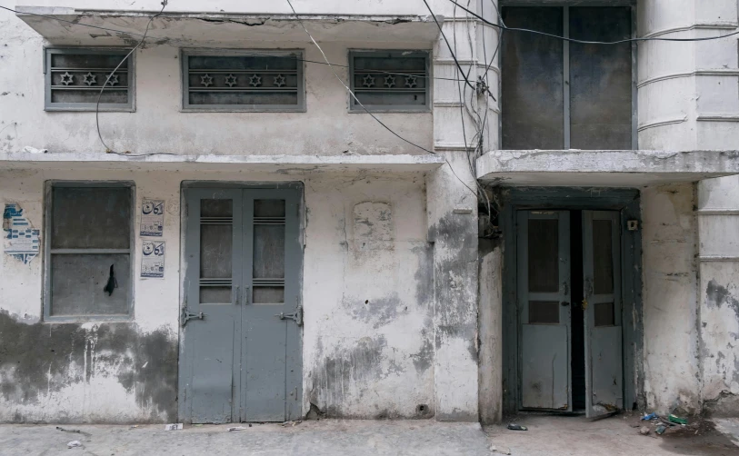 a couple of doors that are on the side of a building, an album cover, by Riza Abbasi, pexels contest winner, whitewashed buildings, government archive photograph, street elevation, grey