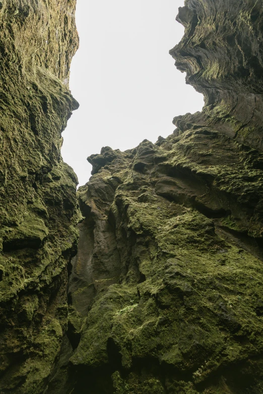 a hole in the side of a mountain with moss growing on it, inspired by Þórarinn B. Þorláksson, unsplash, visual art, tall arches, cavern ceiling visible, tall big rocks, intricate environment - n 9