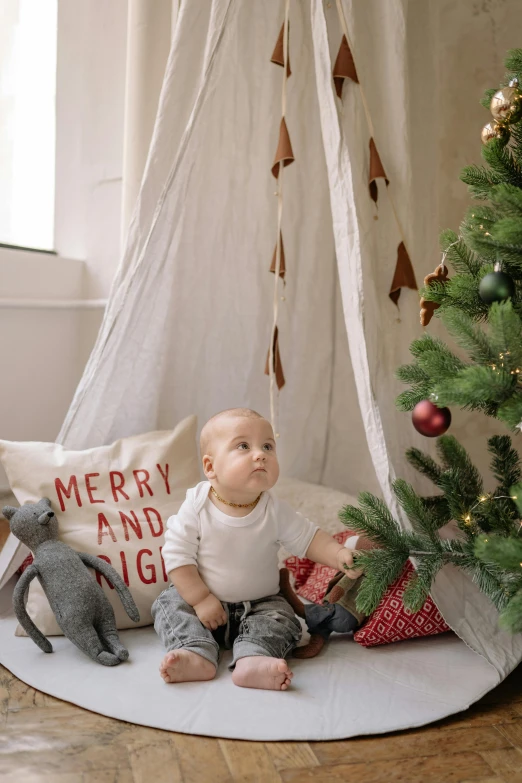 a baby sitting in front of a christmas tree, pexels contest winner, folk art, teepee, high resolution product photo, small, canvas