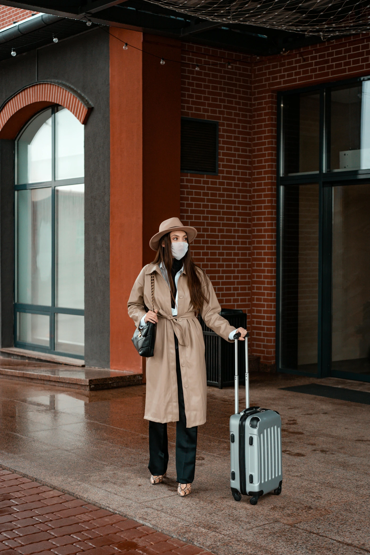 a woman standing in front of a building with a suitcase, wearing a mask, light brown coat, trending on imagestation, hotel room