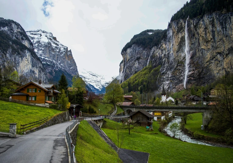 a road going through a valley with mountains in the background, by Julia Pishtar, pexels contest winner, lauterbrunnen valley, multiple waterfalls, whitewashed buildings, lush green