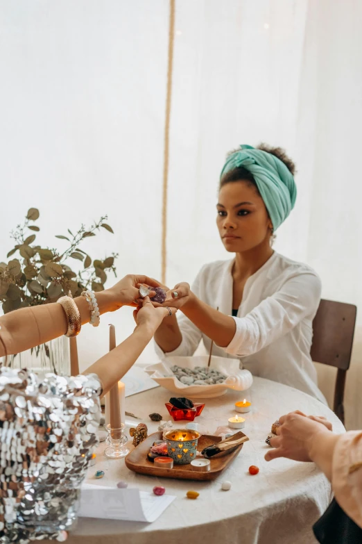 a group of people sitting around a table, wearing a head scarf, candy treatments, sleek hands, thumbnail