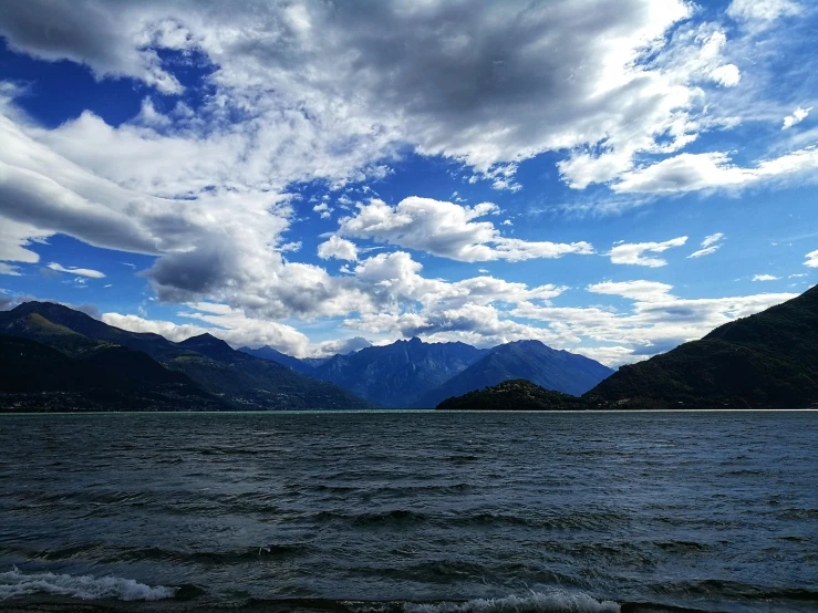 a body of water with mountains in the background, epic blue sky, turbulent lake, the alps are in the background, thumbnail