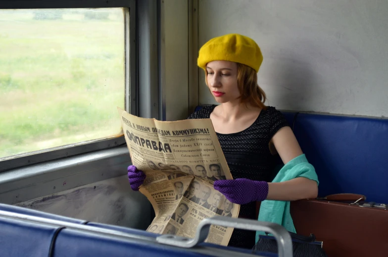 a woman sitting on a train reading a newspaper, by Lucia Peka, yellow cap, russian style, 15081959 21121991 01012000 4k, yellow latex gloves