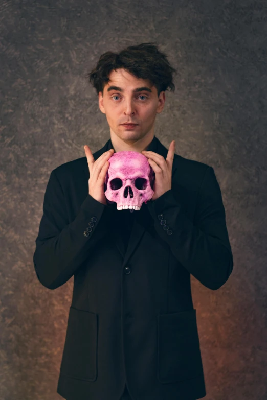 a man holding a pink skull in front of his face, an album cover, by Adam Dario Keel, pexels contest winner, vanitas, timothee chalamet, attractive magician man, ben shapiro, portrait photo of a backdrop