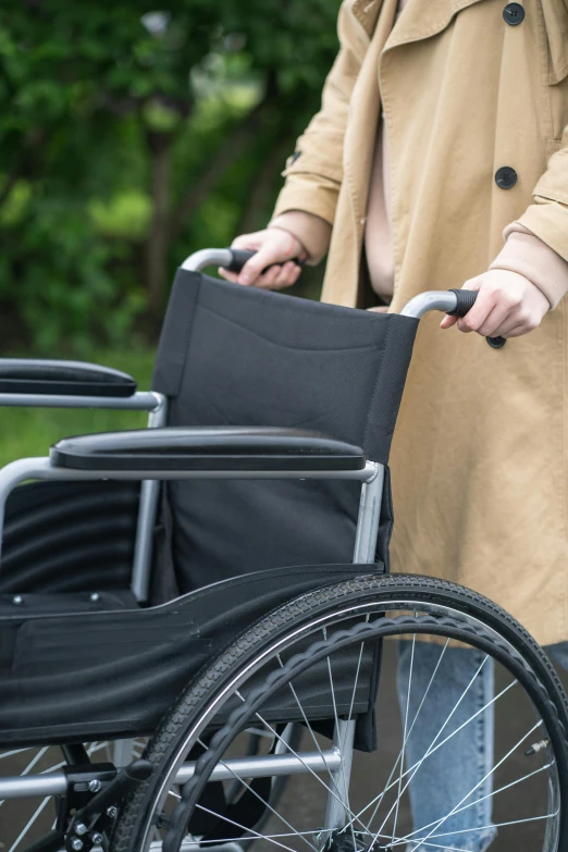 a woman in a trench coat pushing a wheelchair, zoomed in, black, lush surroundings, injured