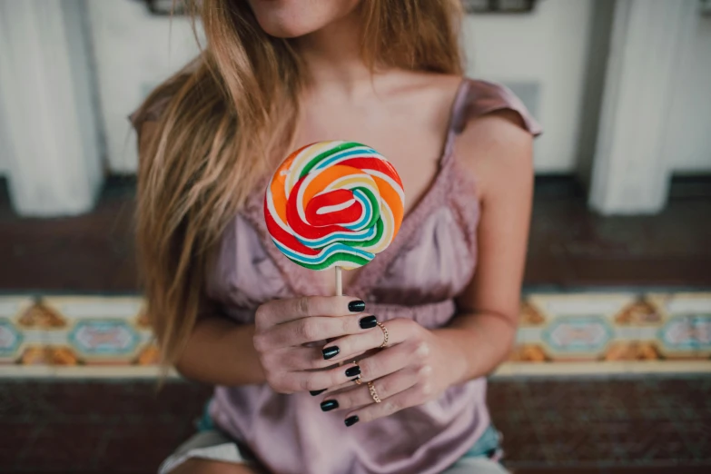 a close up of a person holding a lollipop, by Julia Pishtar, trending on pexels, wearing a cute top, inside an old magical sweet shop, on a canva, instagram model