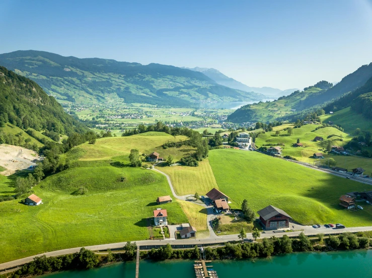 a large body of water next to a lush green hillside, by Franz Hegi, in the swiss alps, lush farm lands, overhead sun, urban surroundings