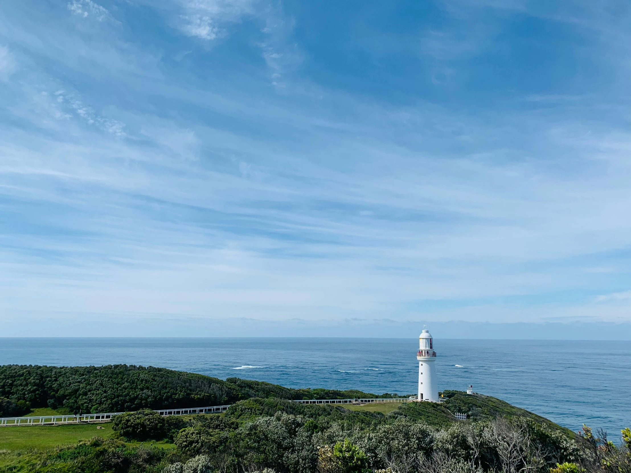 a white lighthouse sitting on top of a lush green hillside, unsplash contest winner, happening, straya, light blue clear sky, touring, coastline