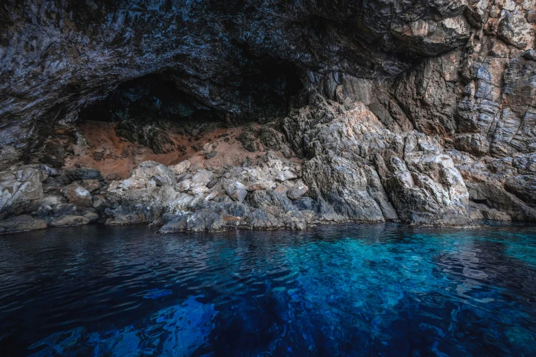 a cave in the middle of a body of water, dark blue water, apulia, promo image, thumbnail