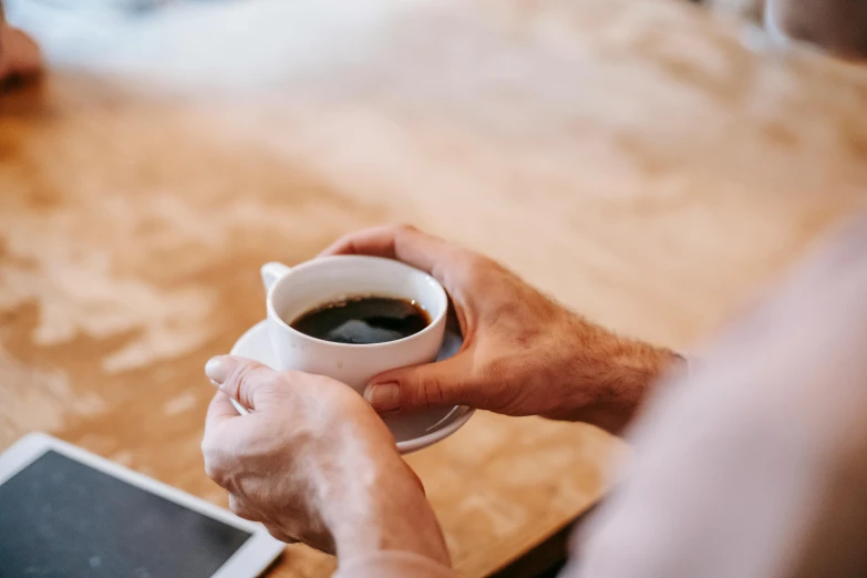 a close up of a person holding a cup of coffee, by Carey Morris, trending on unsplash, sitting on a table, lachlan bailey, multiple stories, slightly muscular