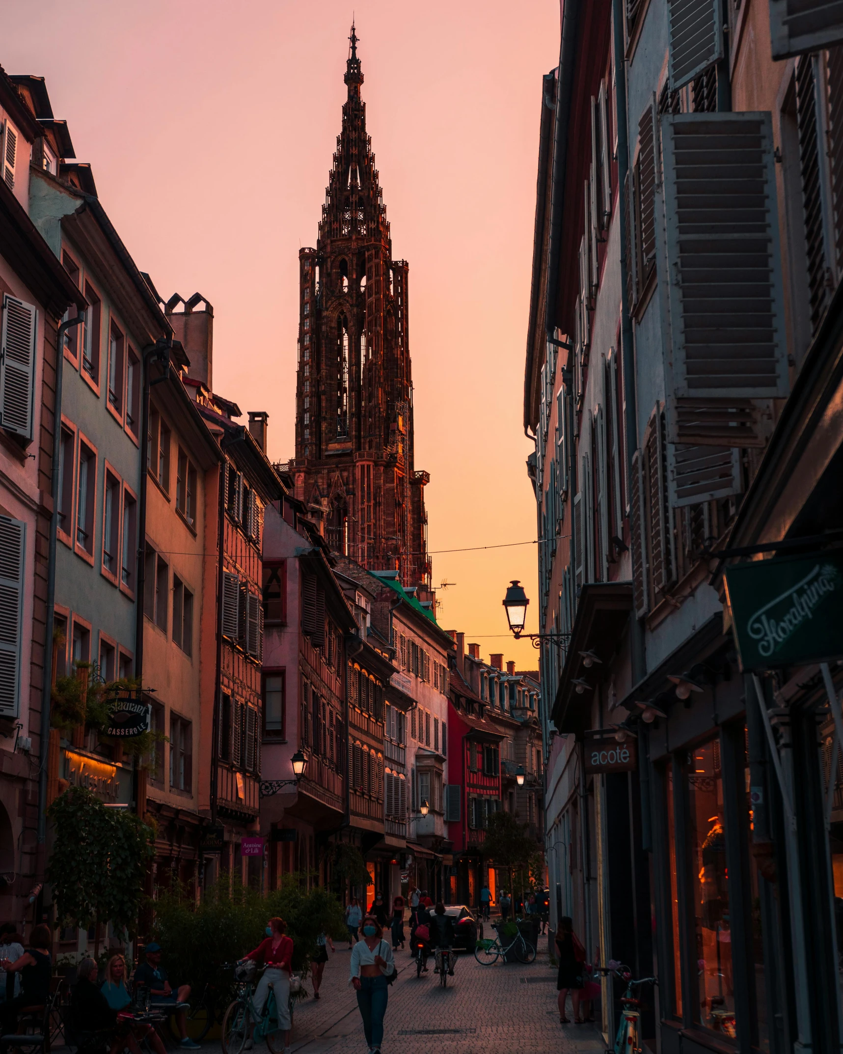 a group of people walking down a street next to tall buildings, by Karl Stauffer-Bern, pexels contest winner, renaissance, pink sunset, french village exterior, brown, good lighted photo