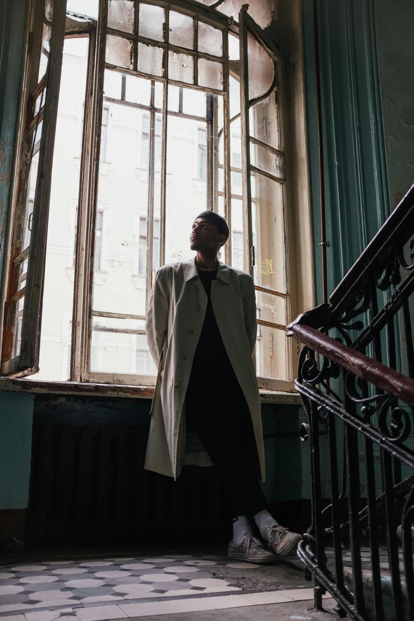 a man standing in front of a window in a building, an album cover, inspired by Dmitry Levitzky, pexels contest winner, ( ( wearing a long coat ) ), ( ( theatrical ) ), androgyny, neo-classicism