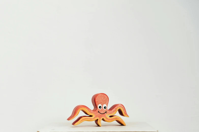 a toy octopus sitting on top of a book, by Okada Hanko, wooden, reddish, multi - coloured, small