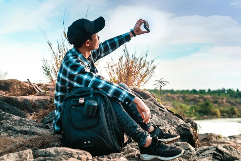 a person sitting on a rock taking a picture, holding a small vape, with a backpack, avatar image, profile photo