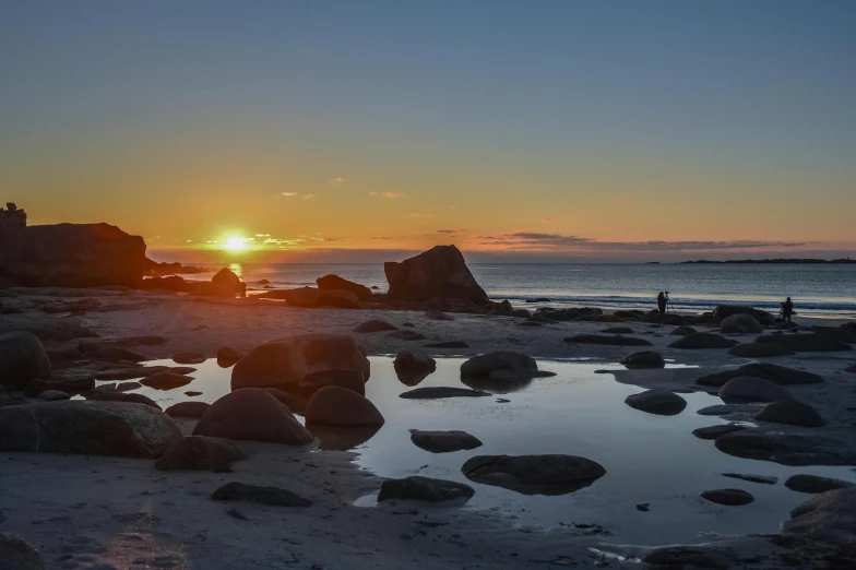 a group of people standing on top of a sandy beach, at the sunset, boulders, rock pools, minna sundberg