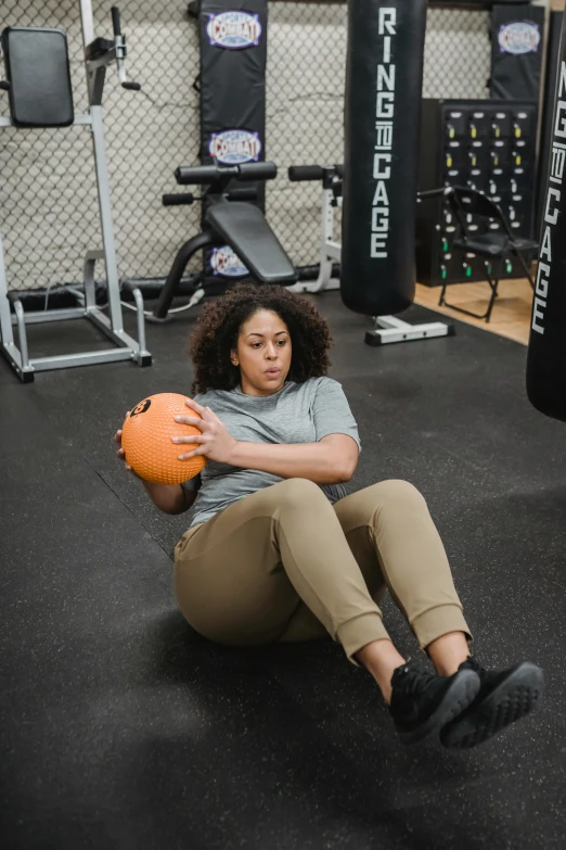 a woman sitting on the ground holding an orange ball, in a gym, curvy build, f/1.4, multiple stories