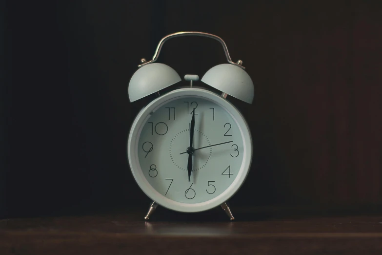 a white alarm clock sitting on top of a wooden table, thumbnail, grey, circular, two