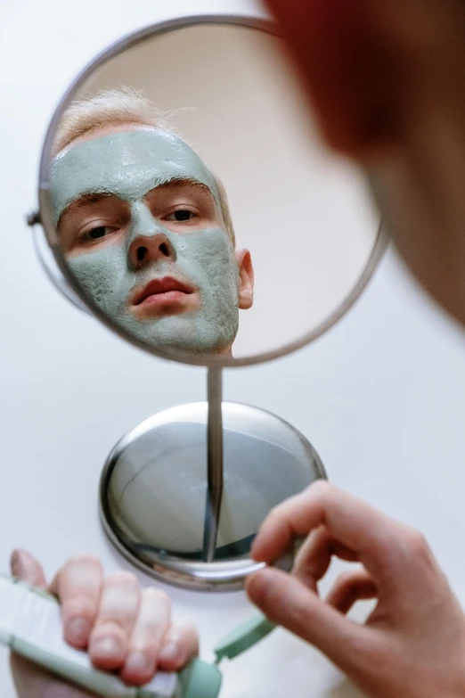 a person brushing their teeth in front of a mirror, by Julian Allen, reddit, green facemask, with grey skin, male model, peeling face skin