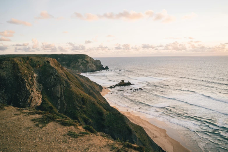 a man standing on top of a cliff next to the ocean, by Carey Morris, pexels contest winner, which shows a beach at sunset, dean cornwall, wide high angle view, soft-sanded coastlines