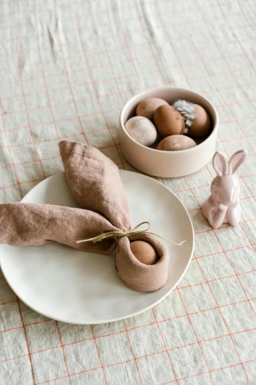 a white plate topped with two napkins next to a bowl of eggs, by Henriette Grindat, unsplash, mingei, covered with pink marzipan, made of clay, thumbnail, brown