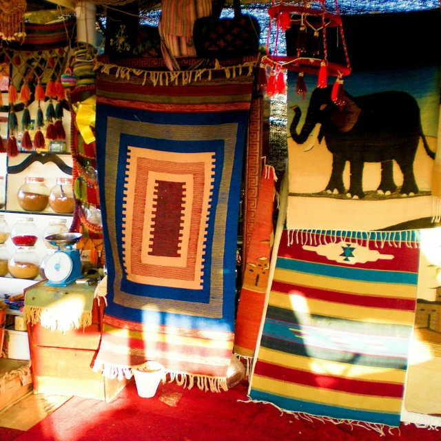 a store filled with lots of different types of rugs, by Phyllis Bone, in a colorful tent, warm sunlight shining in, patagonian, maroon and blue accents