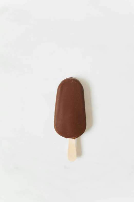 a chocolate ice cream bar sitting on top of a white counter, smooth oval head, 20mm, poppy, straight smooth vertical