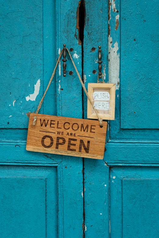 a blue door with a sign that says welcome to the open, a stock photo, pexels, folk art, square, brown, programming, on a wooden tray