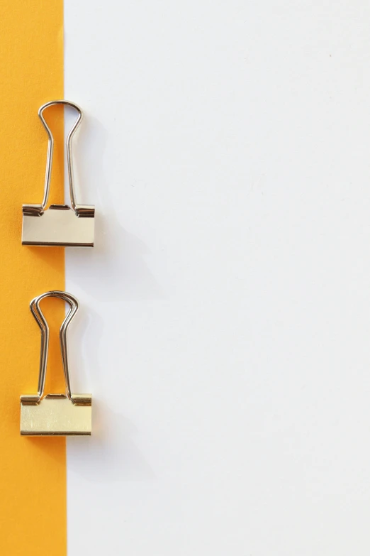 three paper clips on a yellow and white background, by Julian Allen, trending on pexels, padlocks, two hang, on a white table, detailed product image