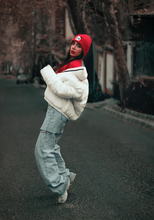 a woman standing in the middle of a street, an album cover, inspired by Elsa Bleda, trending on pexels, graffiti, red cap, attractive pose, white puffy outfit, winter season