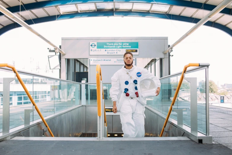 a man in a space suit standing on an escalator, an album cover, inspired by Jules Tavernier, pexels contest winner, happening, pendleton ward, lunar themed attire, heath clifford, monorail station