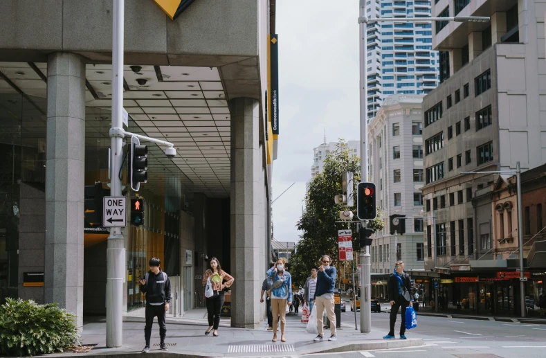 a group of people walking down a street next to tall buildings, by Lee Loughridge, pexels contest winner, happening, manuka, intersection, non-binary, overwatch building