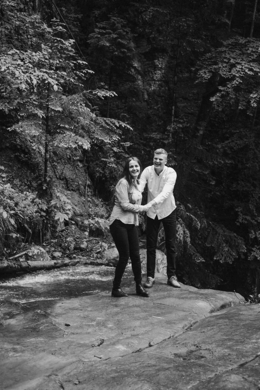 a man and woman standing in front of a waterfall, a black and white photo, enjoying a stroll in the forest, liam, both smiling for the camera, about to step on you