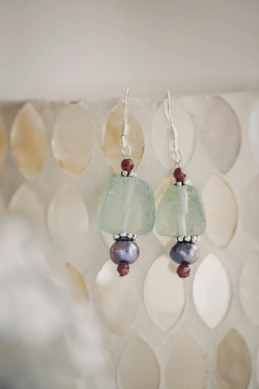 a close up of a pair of earrings on a table, a picture, inspired by Perle Fine, seaglass, maroon, peru, pearls and oyesters