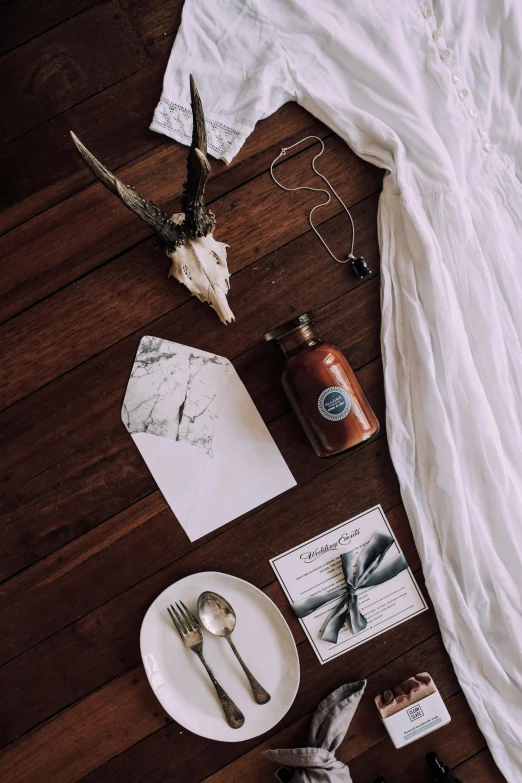 a white dress sitting on top of a wooden floor, a still life, by Sydney Carline, unsplash contest winner, renaissance, cow skull, invitation card, strange ingredients on the table, brown and white color scheme